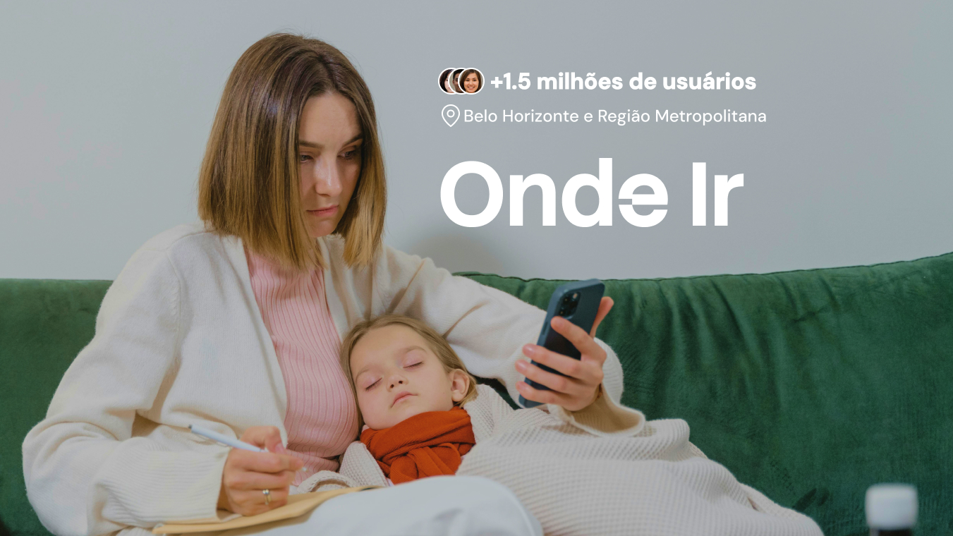 Mãe de pijamas, sentada no sofá com a filha pequena no colo adormecida, olhando o celular procurando informações de saúde